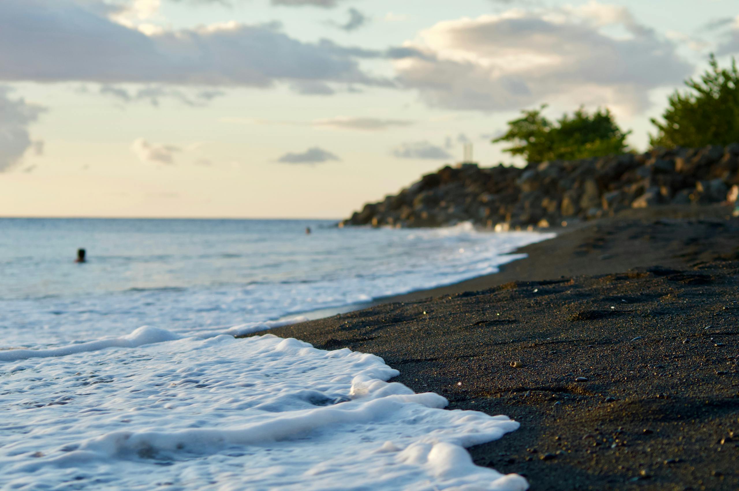 Calm ocean waves on a black sand beach in Guadeloupe with a serene sunset backdrop.